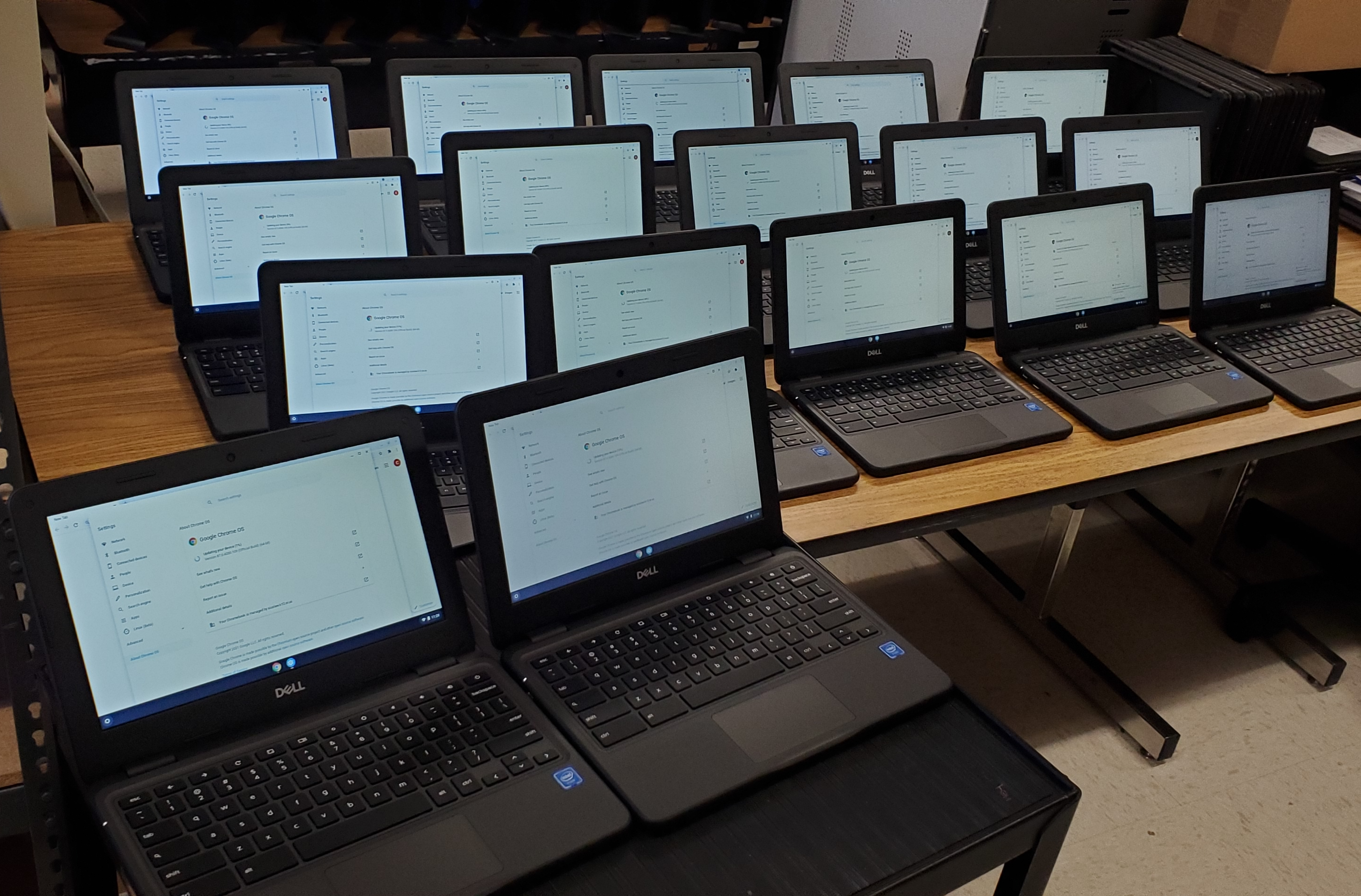 17 Chromebooks  that are open and on displaned lined up on a cart and large table. 
