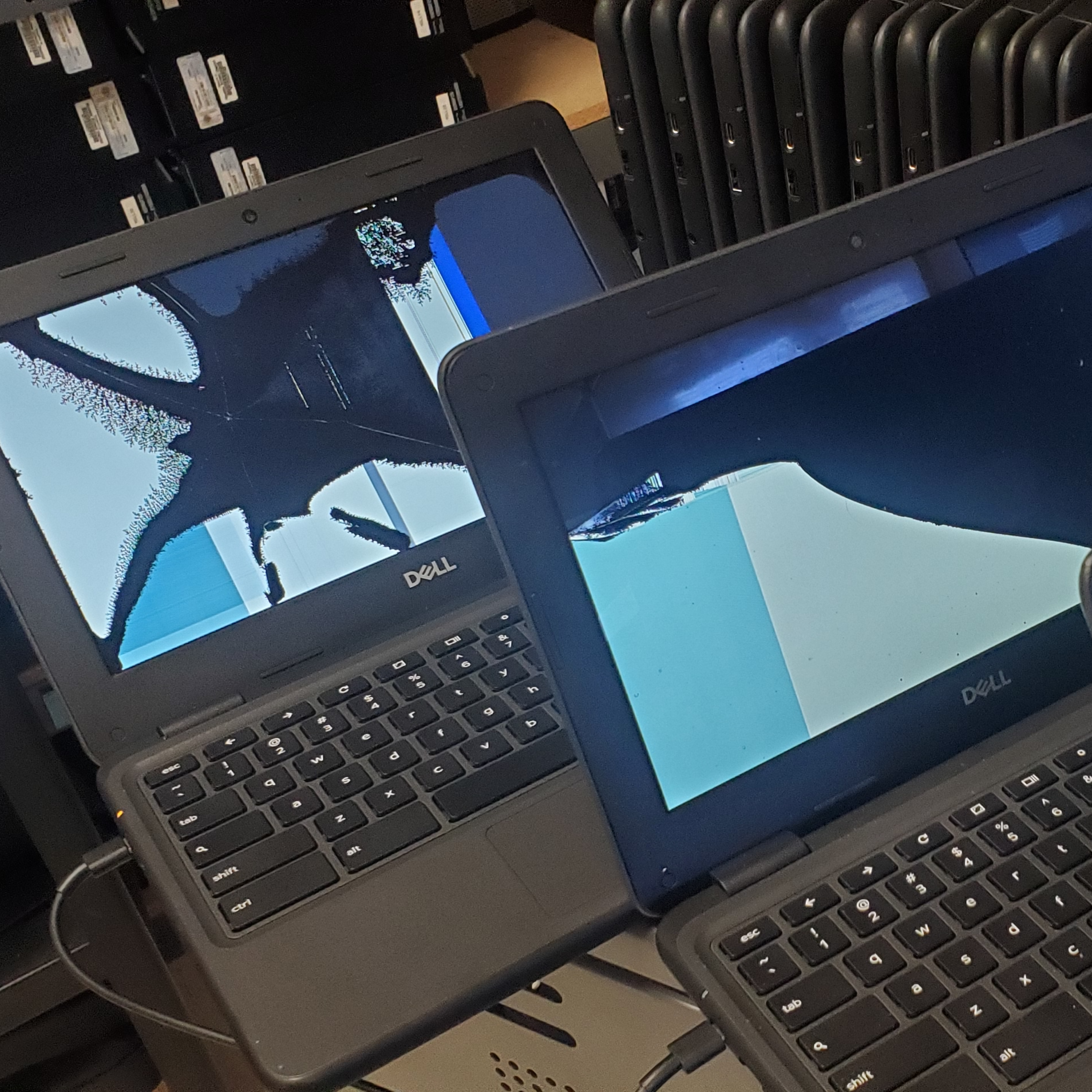 2 Dell laptops turned on with some laptops surrounding them.
