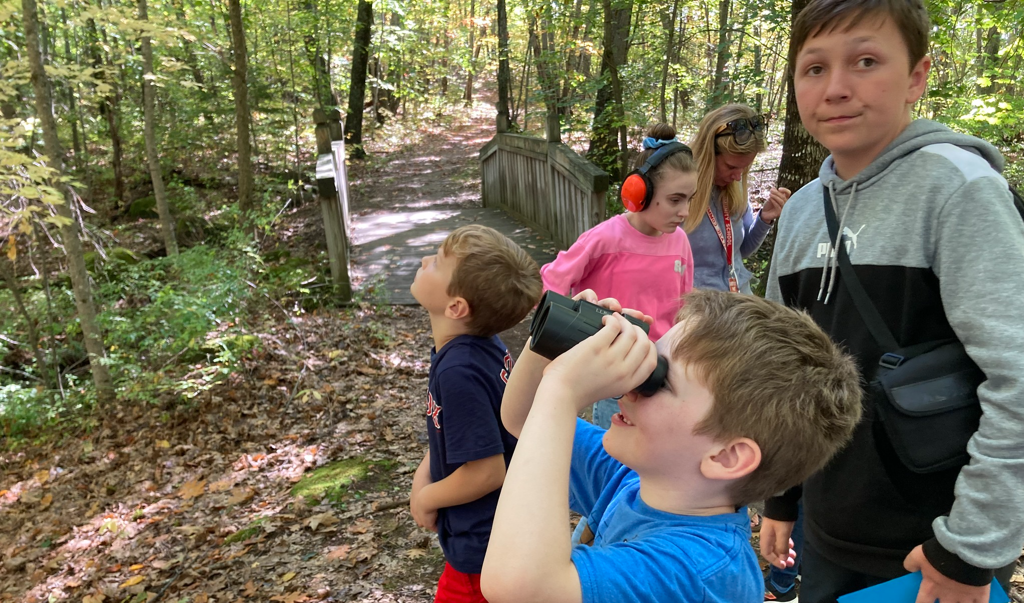 Students on a walking trail in the woods next to a wooden bridge. 