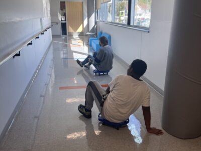 students riding boogie boards on wheels in the hall