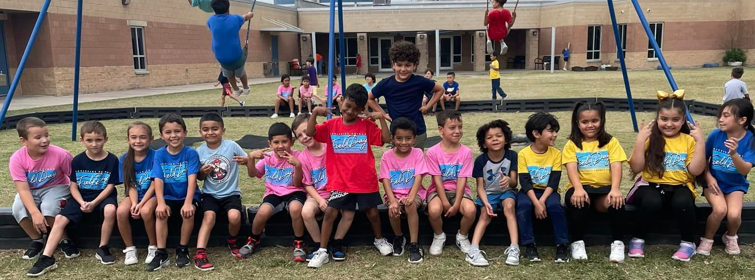 Students sitting in a line on a low ledge on the playground