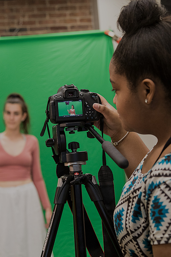  A Student filming another in a green screen using a camera