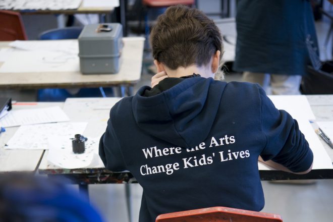 Kid wearing a hoodie that says "Where the Arts Change Kids' Lives"