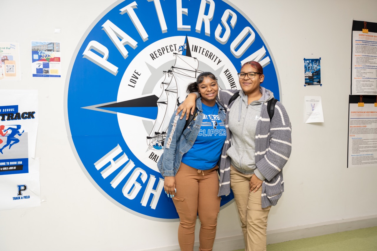 Two students pose for a picture in front of Patterson high school mural