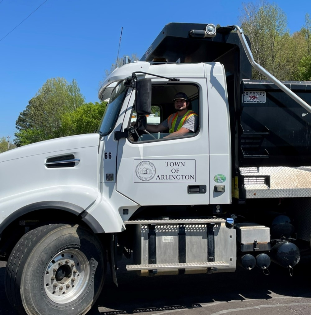 White cab of a large commercial truck with Public Works logo on side and smiling employee in driver's seat