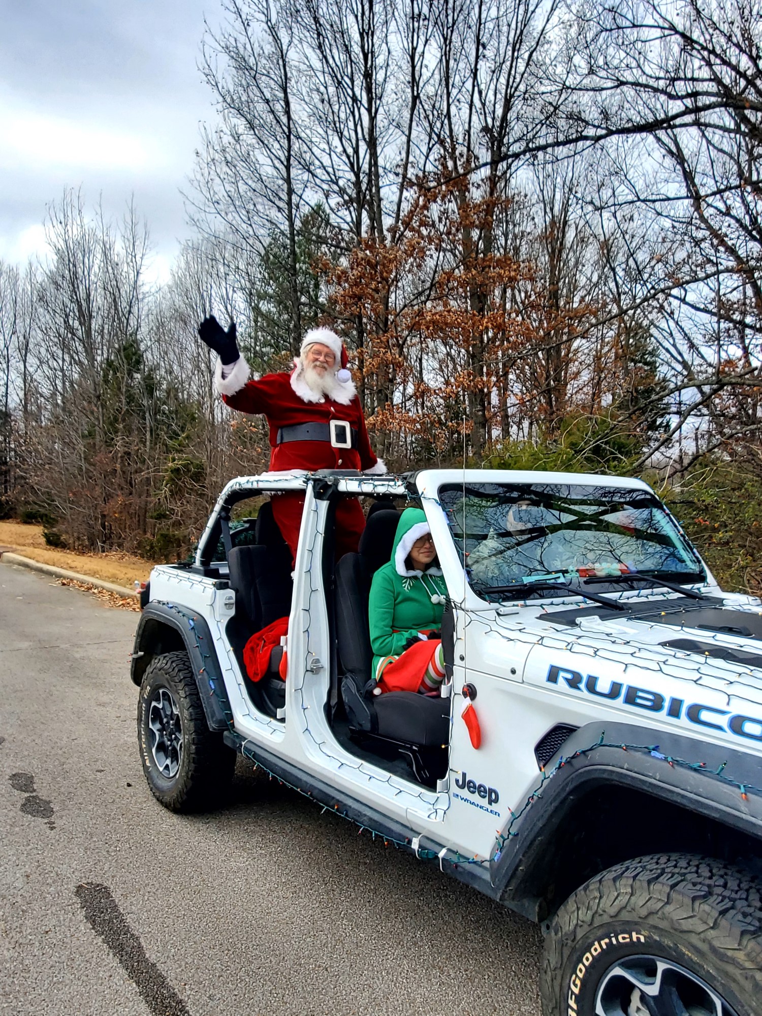 Santa Clause waving from the back seat of a white, open top jeep