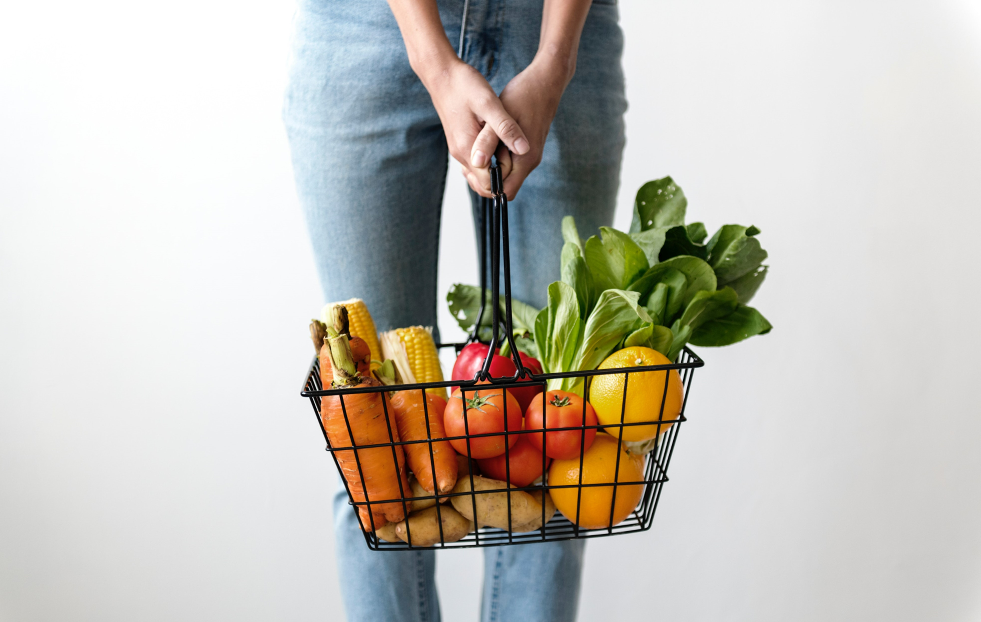 picture of a lady holding a metal basket full of produce, from waist down