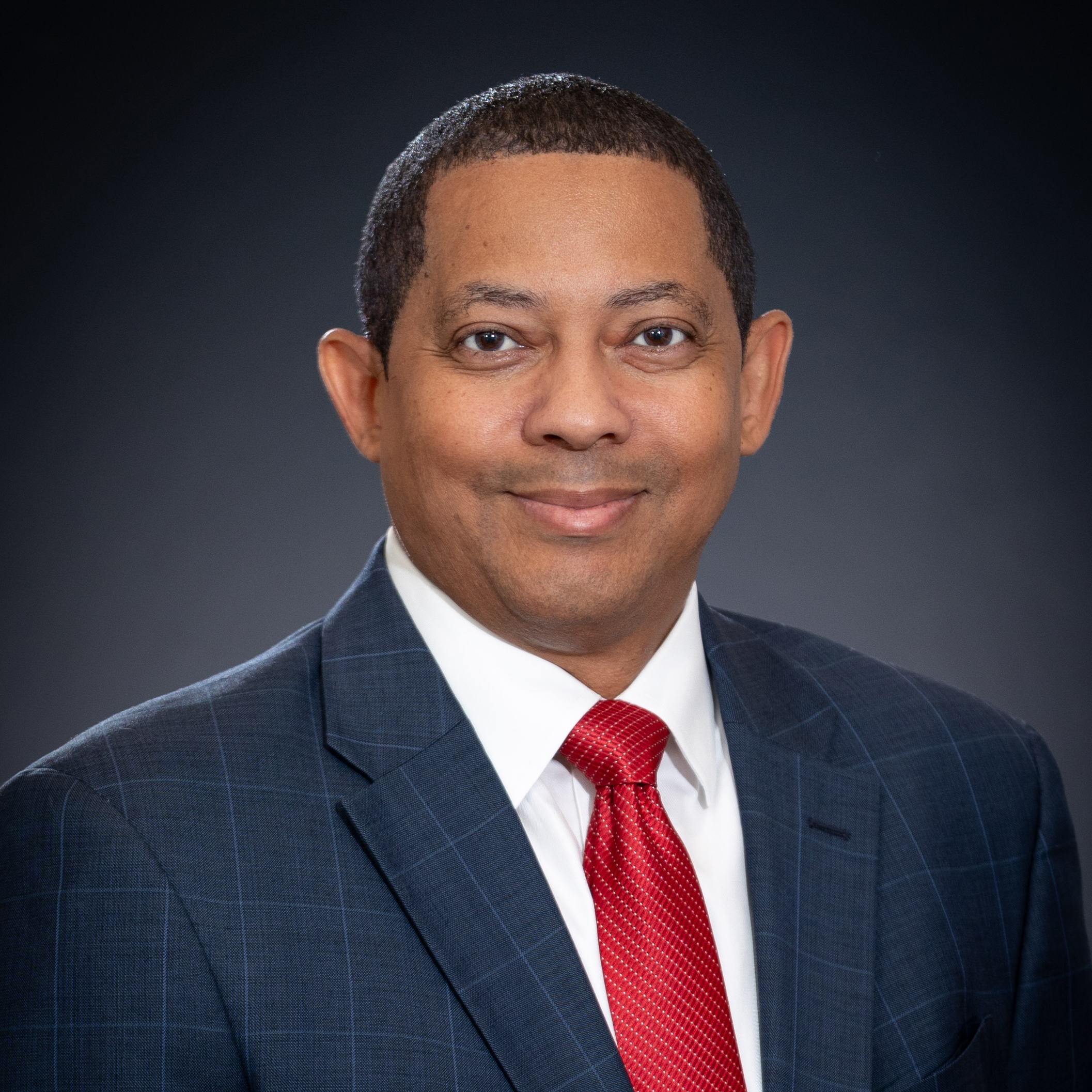 Headshot of Alderman Dwight Barker in gray suit, white shirt, and red tie