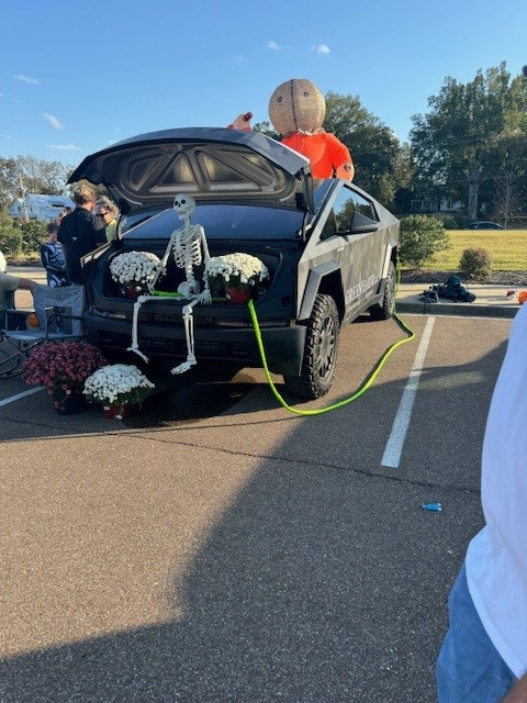 Trunk of a car decorated for Trunk or Treat event with a skeleton sitting between two white mums