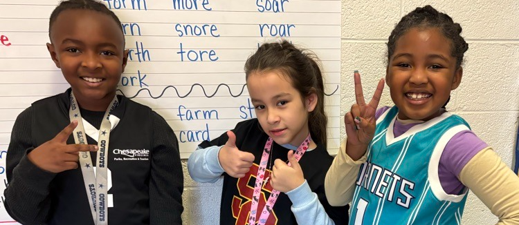 students give thumbs up and peace signs with their hands while wearing jerseys for a Sports-themed spirit day