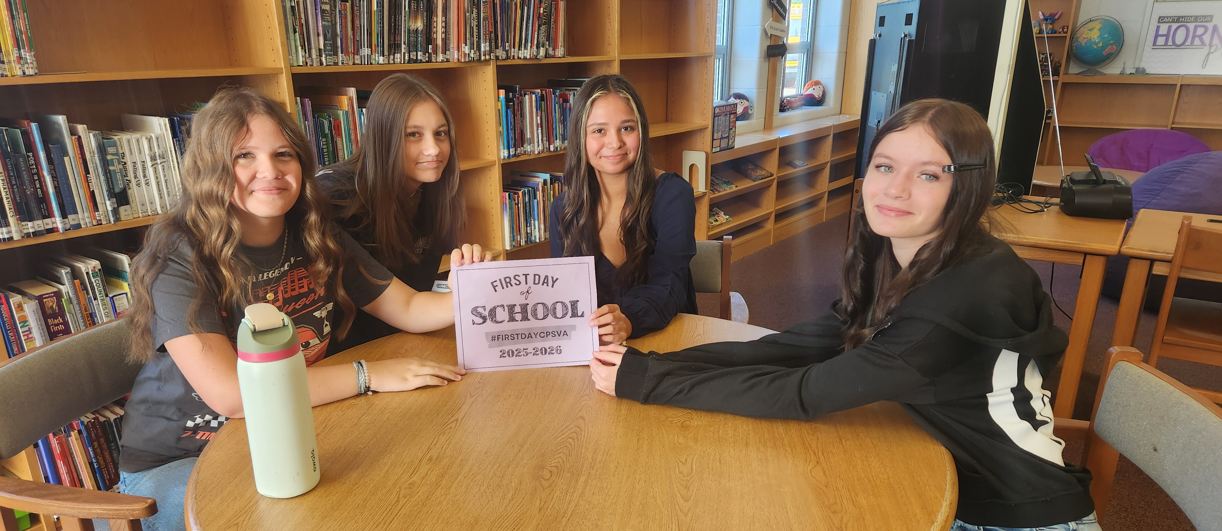 Four girls holding up a sign that says First Day CPS Schools Sign. They are in the library.