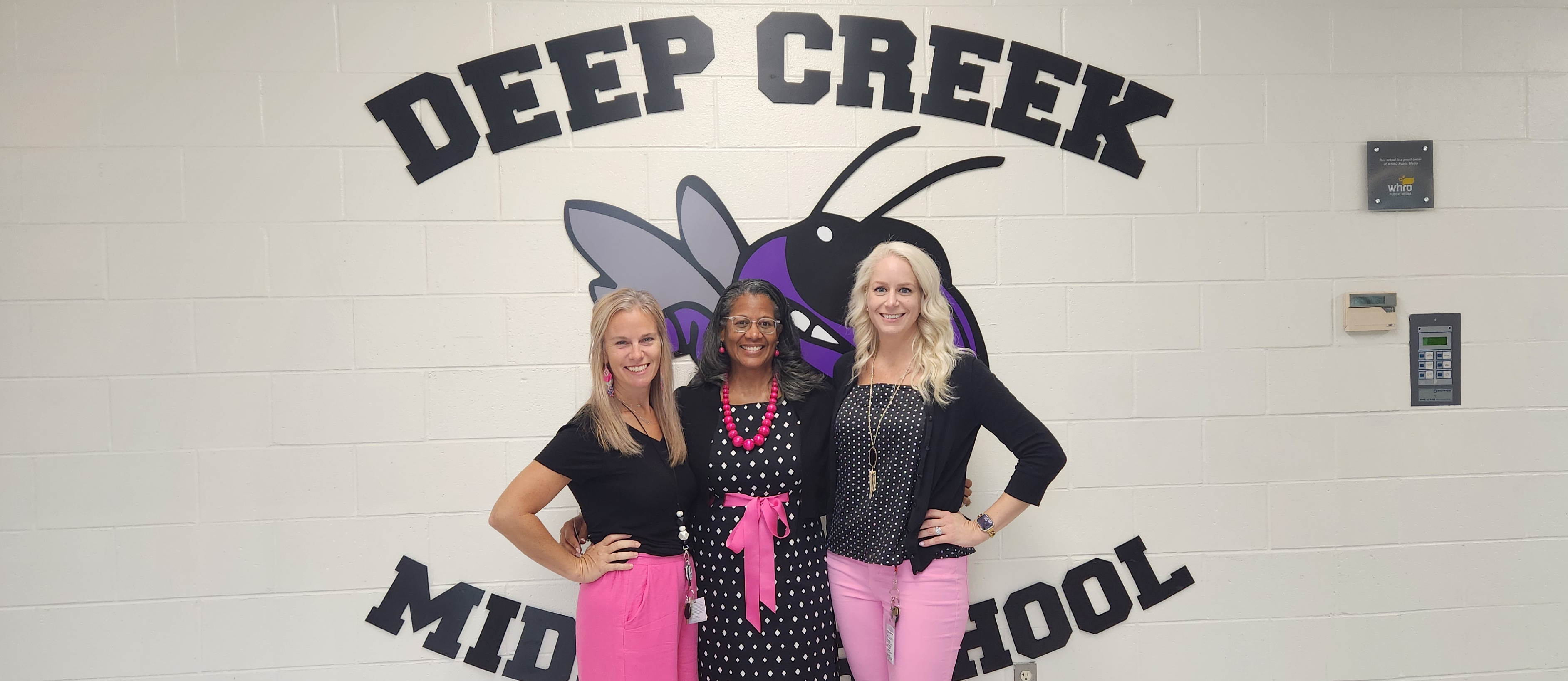 Mrs. Doran, Mrs. Davenport, and Mrs. Dangerfield wearing pink in front of the DCMS sign