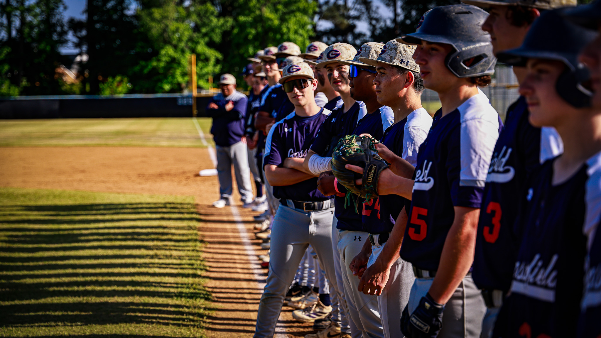 A GFH baseball player poses for the camera while the team lines up for the national anthem