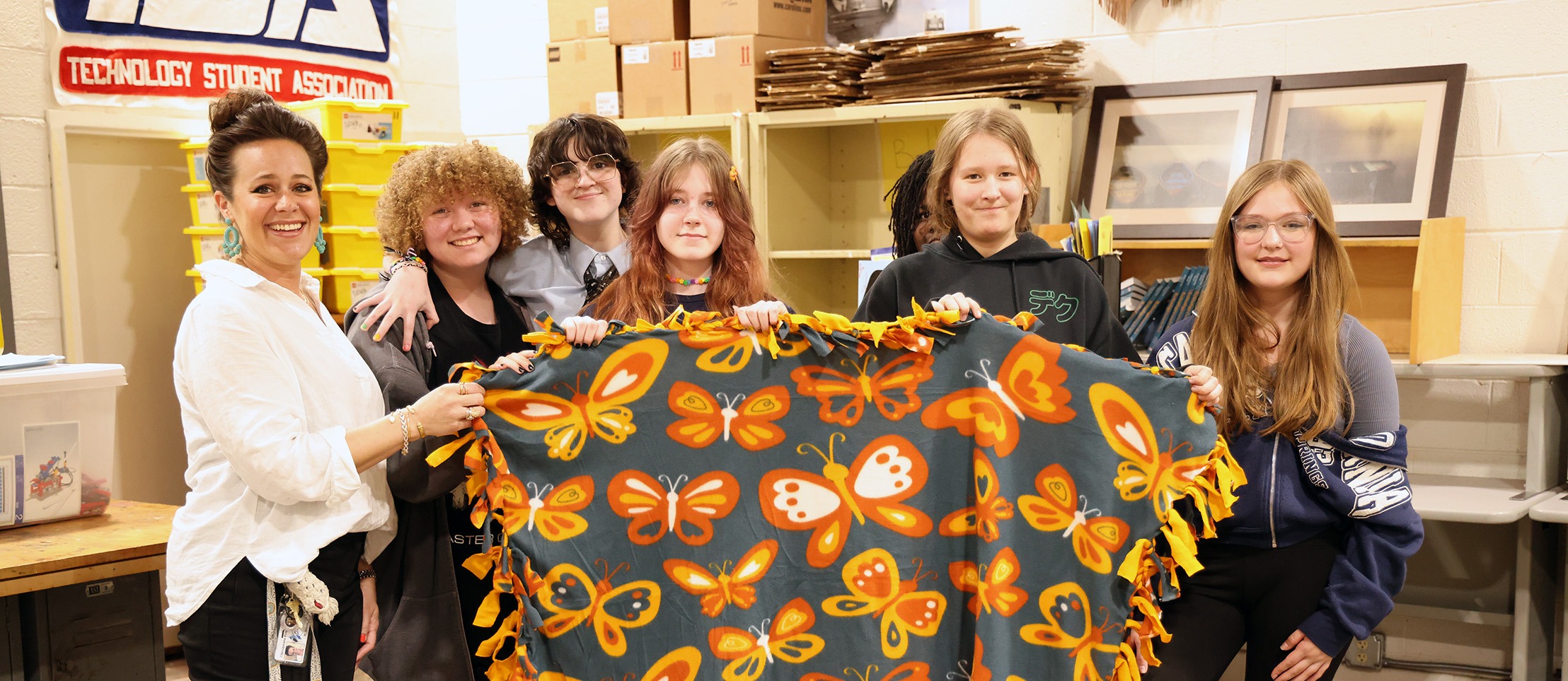Students and teacher hold up a blanket they made for a charity