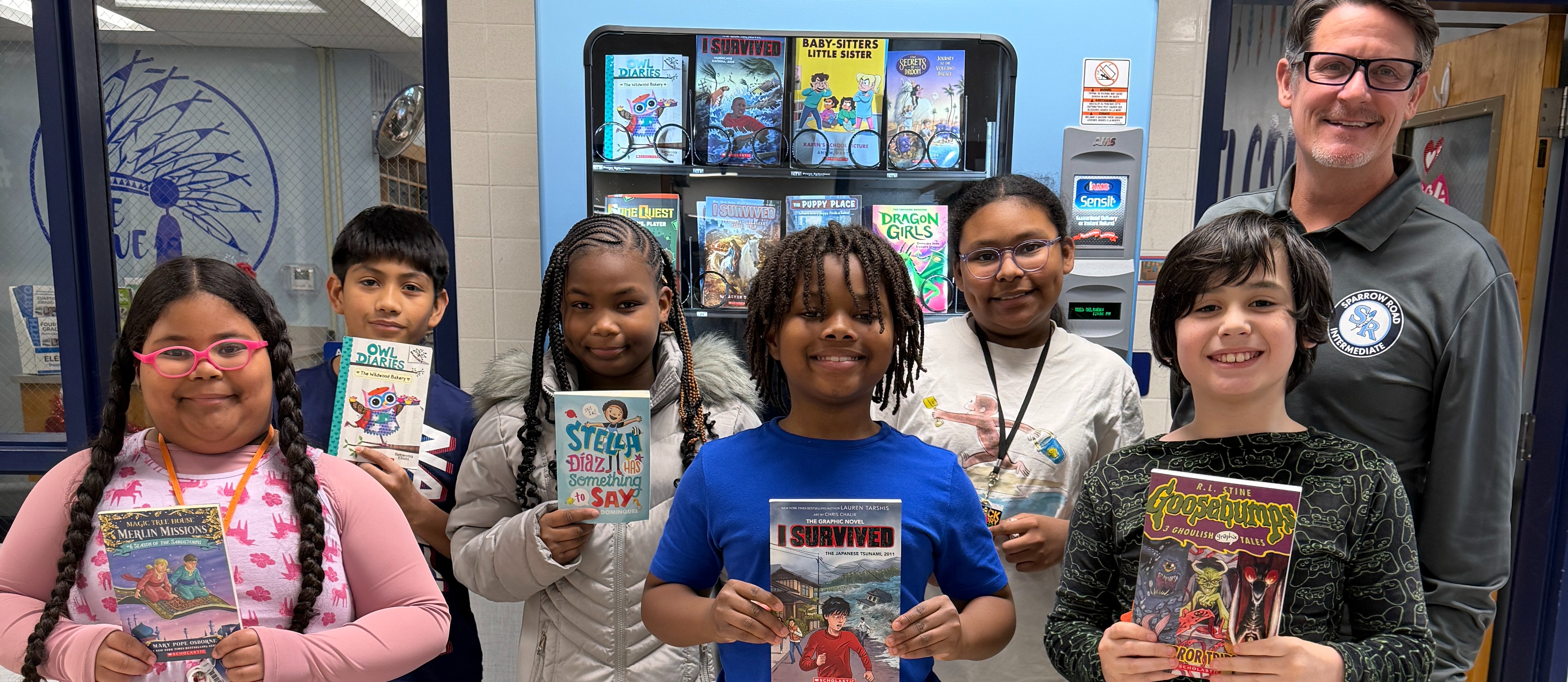Students earned books from the book vendering machine and are holding them up with Mr. Triolet for Character Counts at SRI.