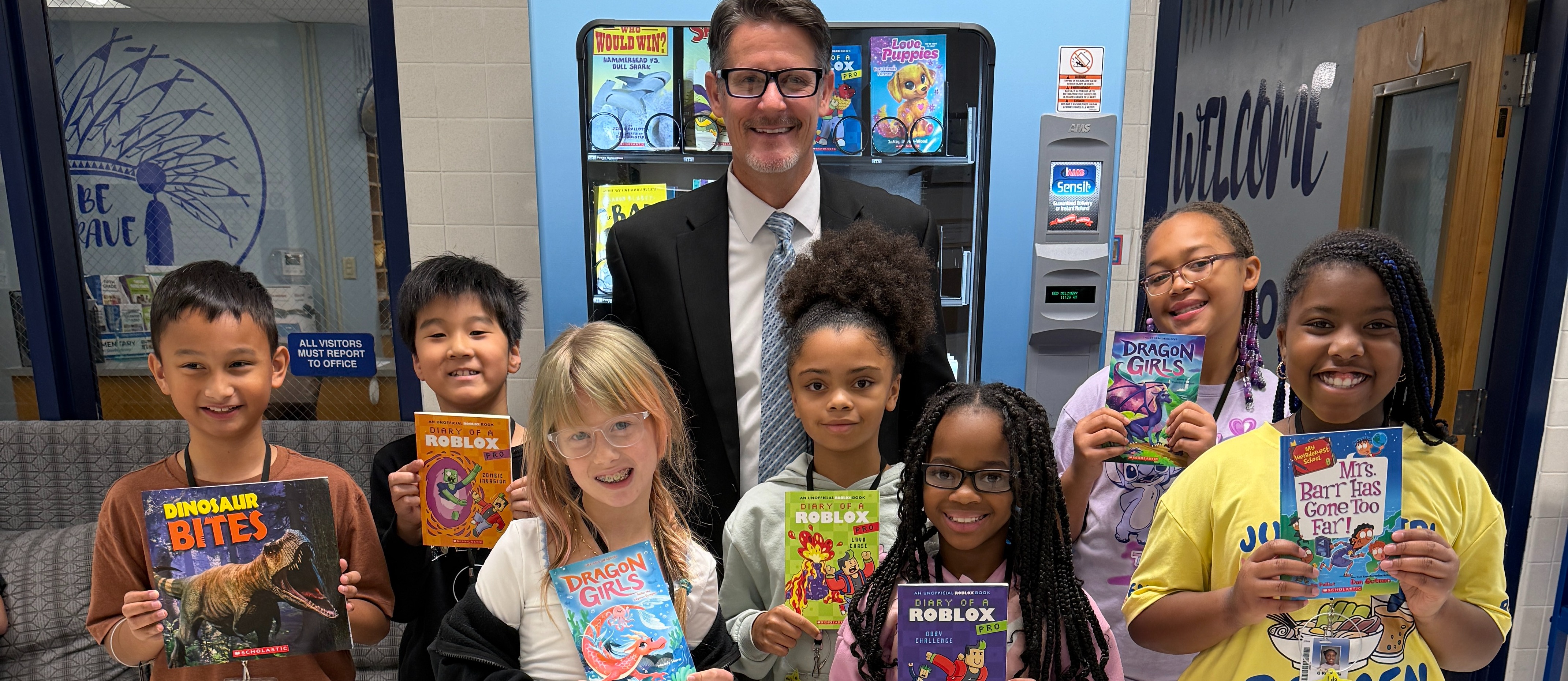 Students holding up books with Mr. Triolet in front of the book vending machine.