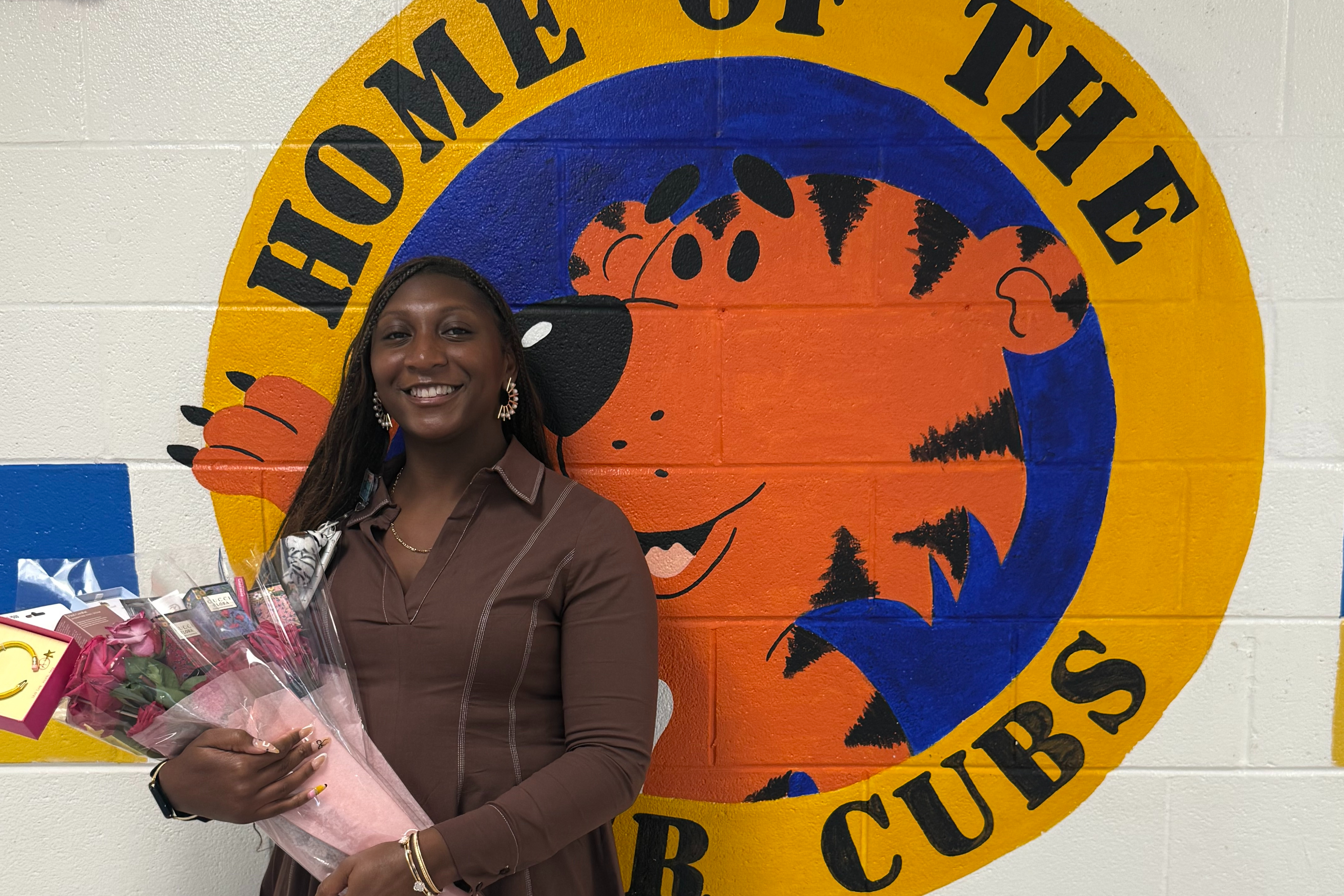 Our teacher of the year, Ms. Robinson, holding a pink bouquet in front of a Home of the Tiger Cubs logo.