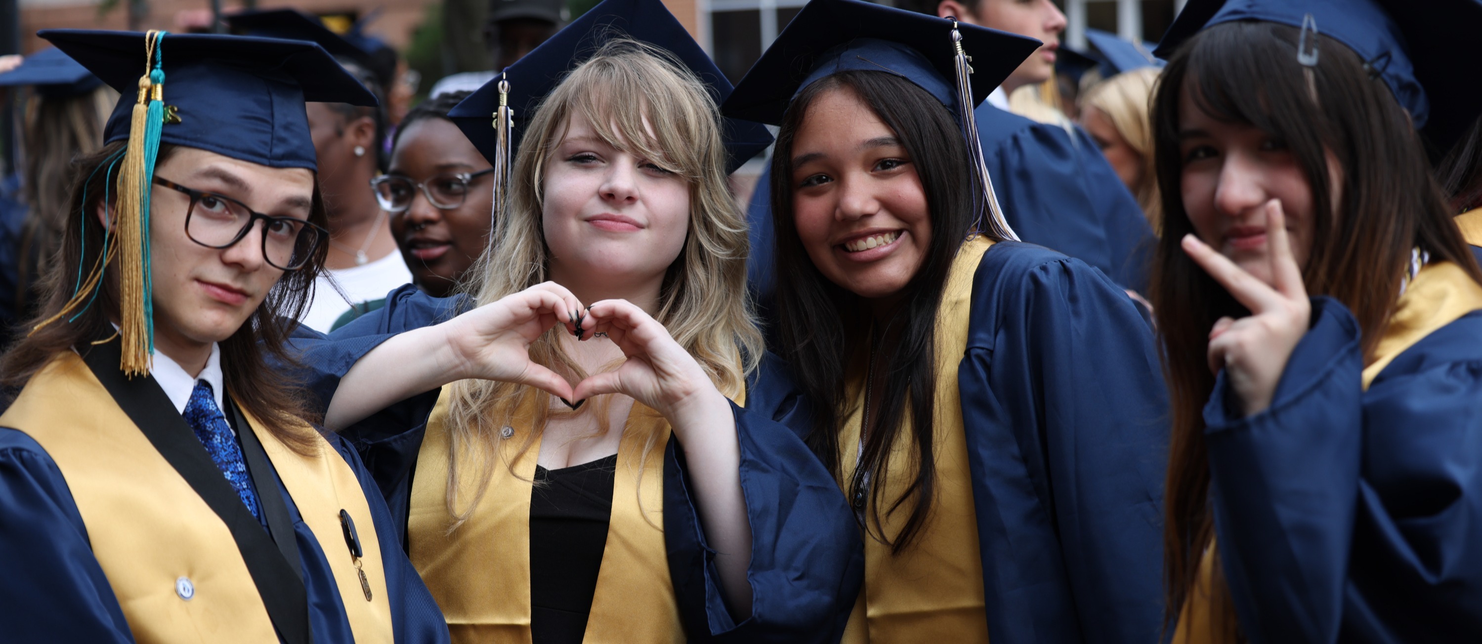 Four graduates in blue caps and gowns with gold stoles pose together and smile during the Western Branch High School graduation ceremony.