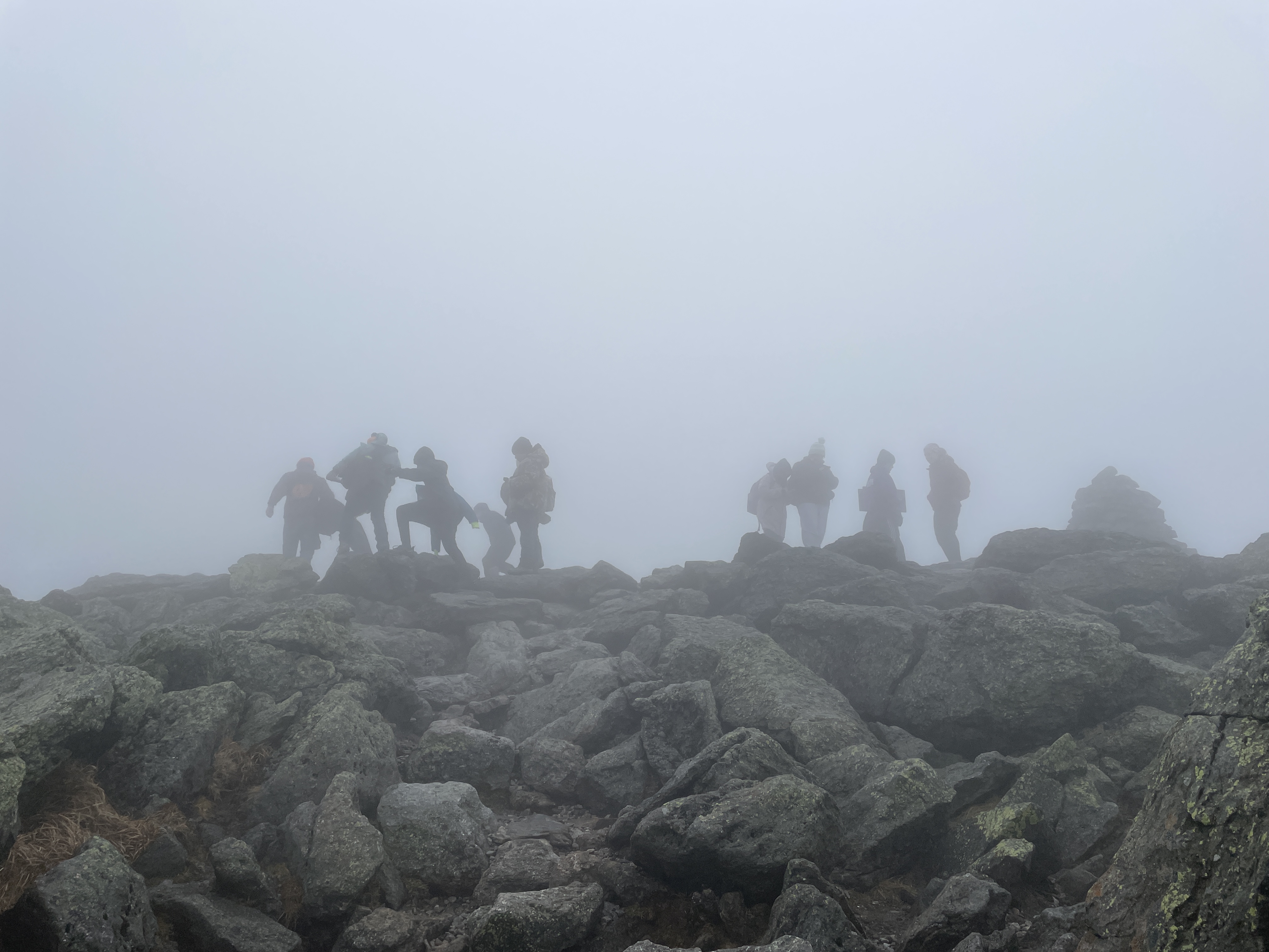 Students walk across rock summit of Mt. Washington in the fog. 