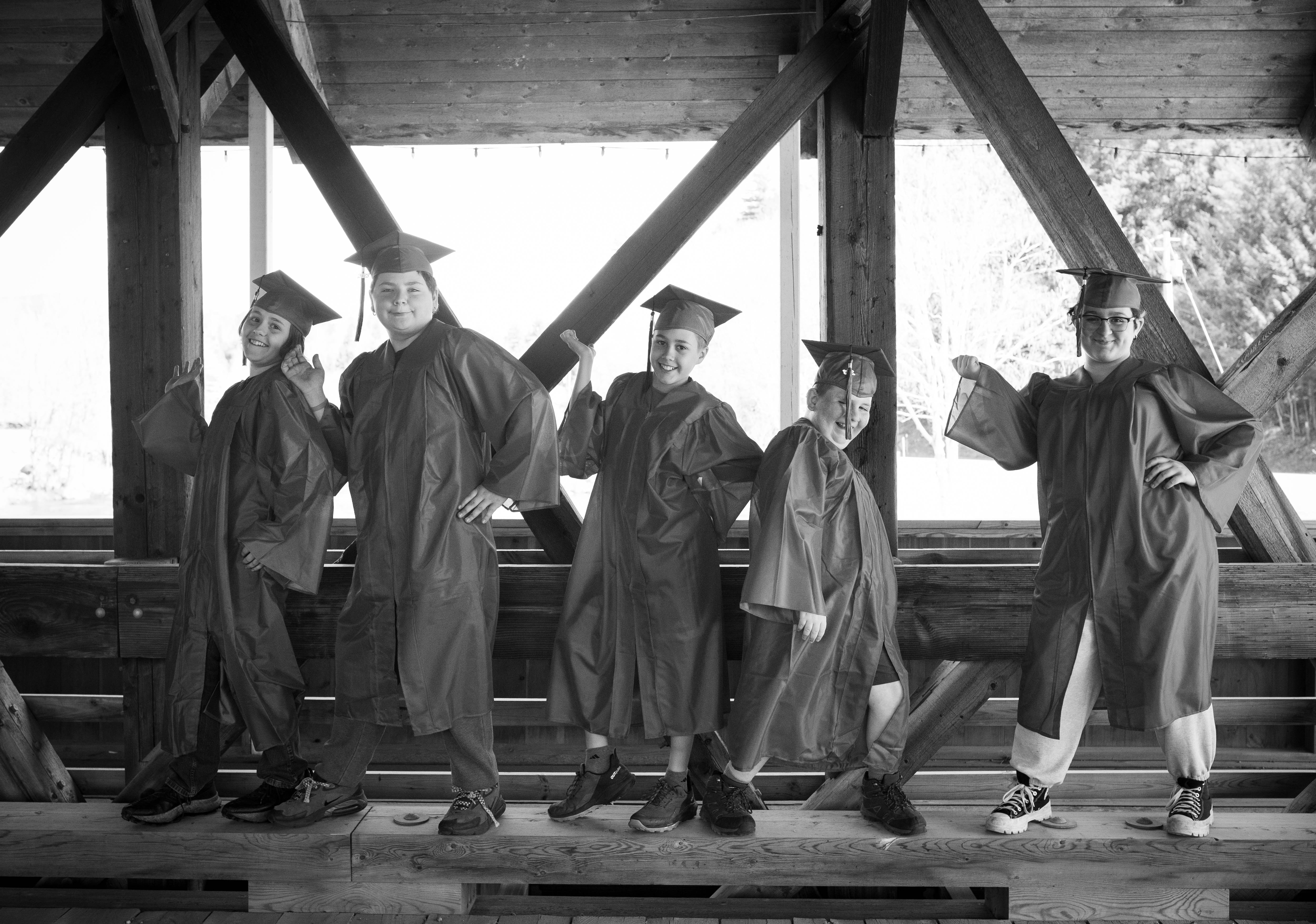 Five Graduate strike funny poses while wearing their caps and gowns. 