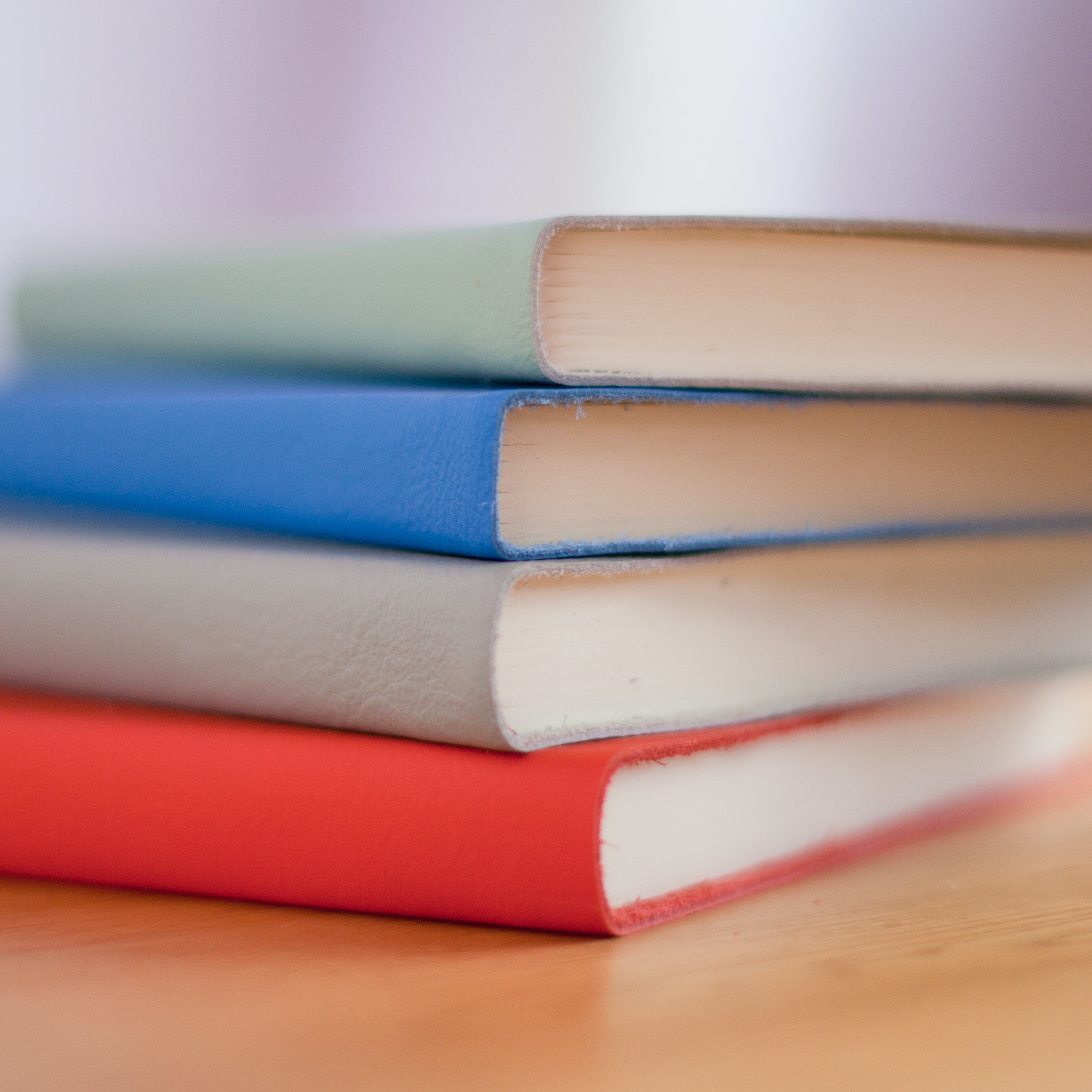 Four books in red, gray, blue, and green stacked on a wooden table with a soft background.