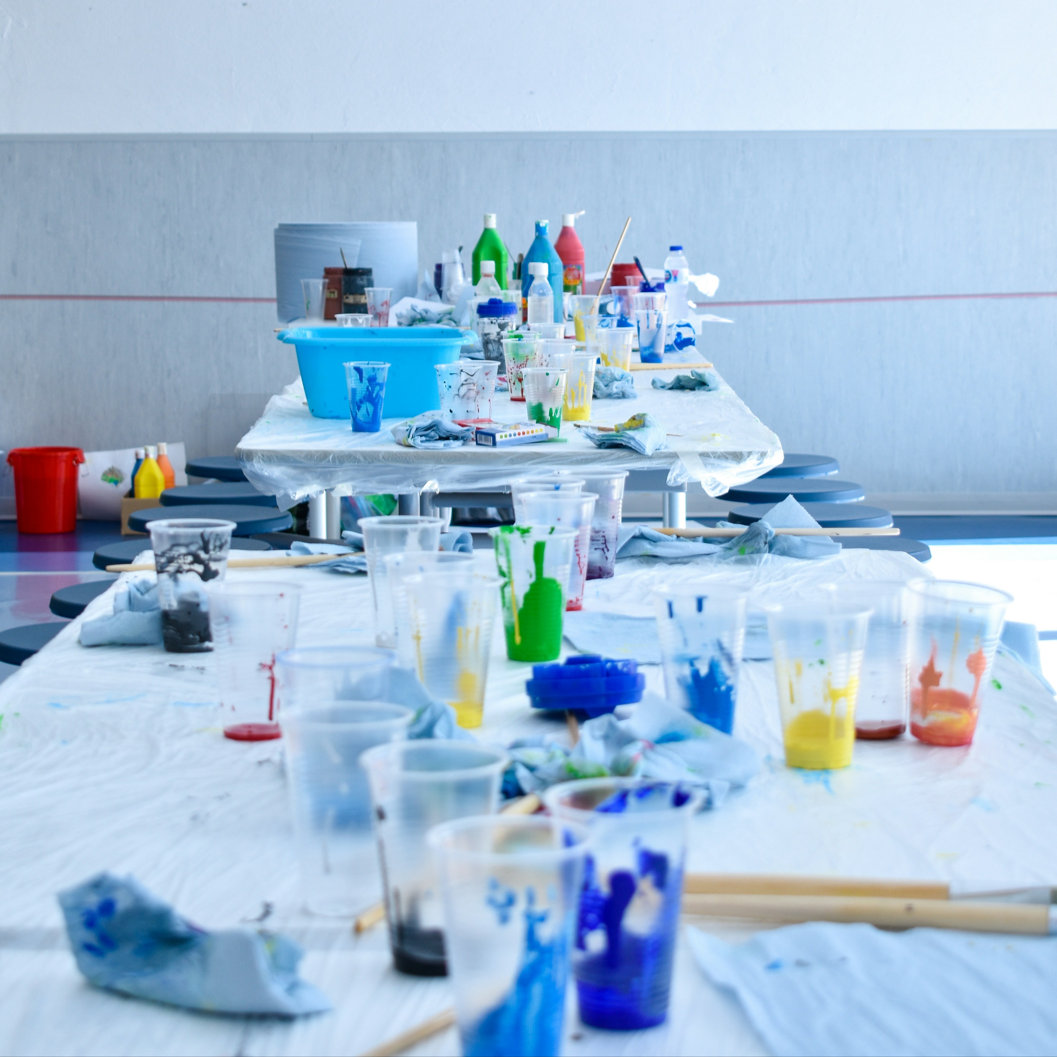 An art studio with tables holding paint cups and brushes. The walls are white and the floor is blue.