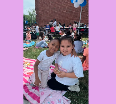 two children having a picnic outside.  They are hugging and one is holding a hamburger