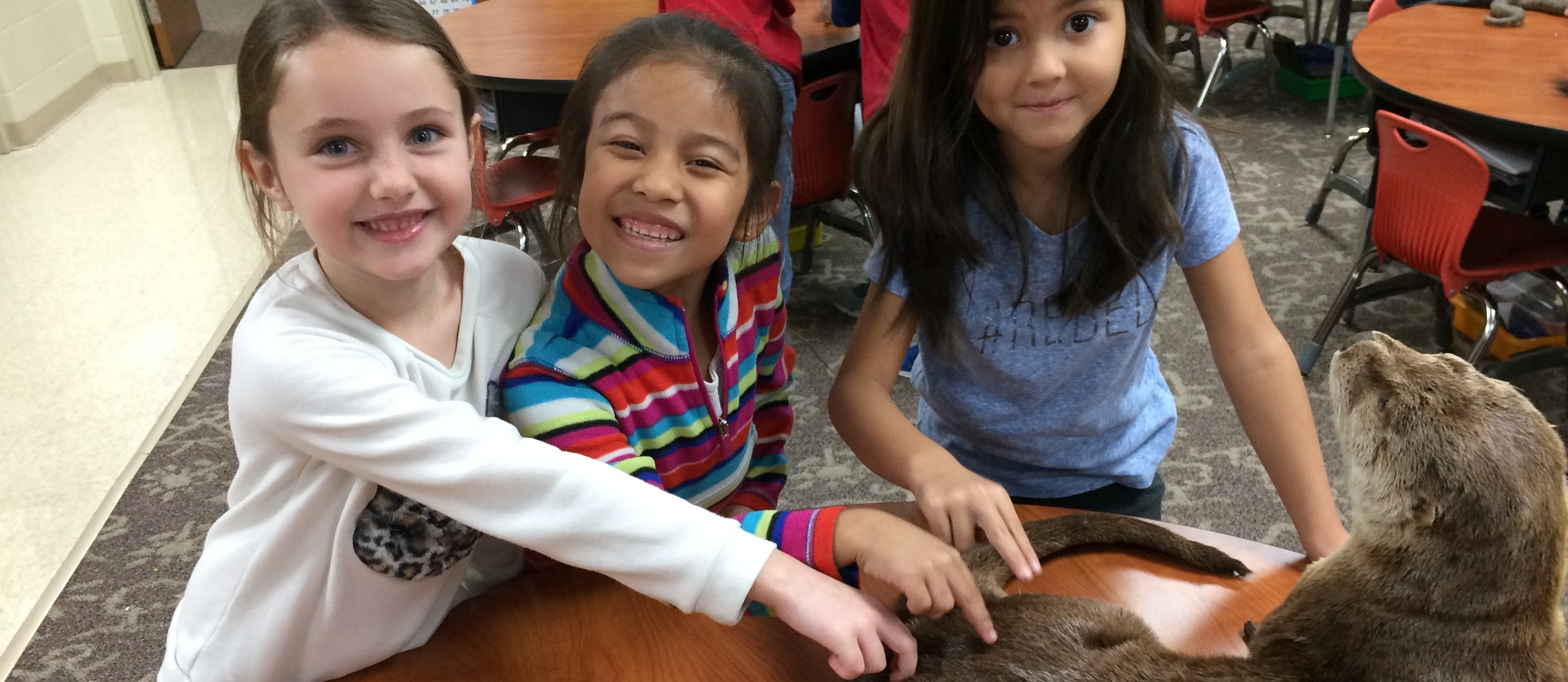 Three student smile while petting stuffed otter