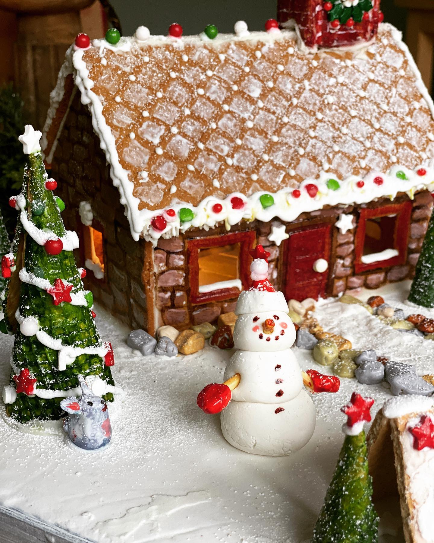 a snowy cottage gingerbread house with a fondant snowman in front