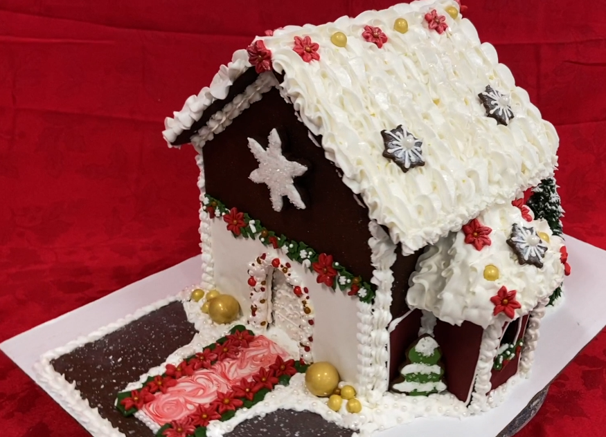 a dark brown gingerbread house on a red tablecloth