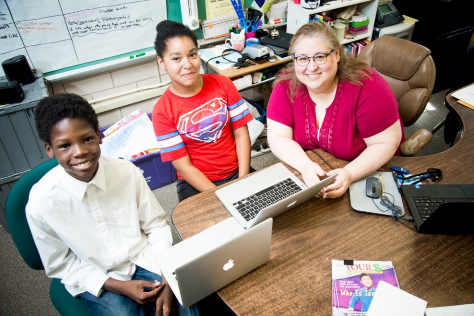 Two young teens and a teacher using laptops sitting on a desk