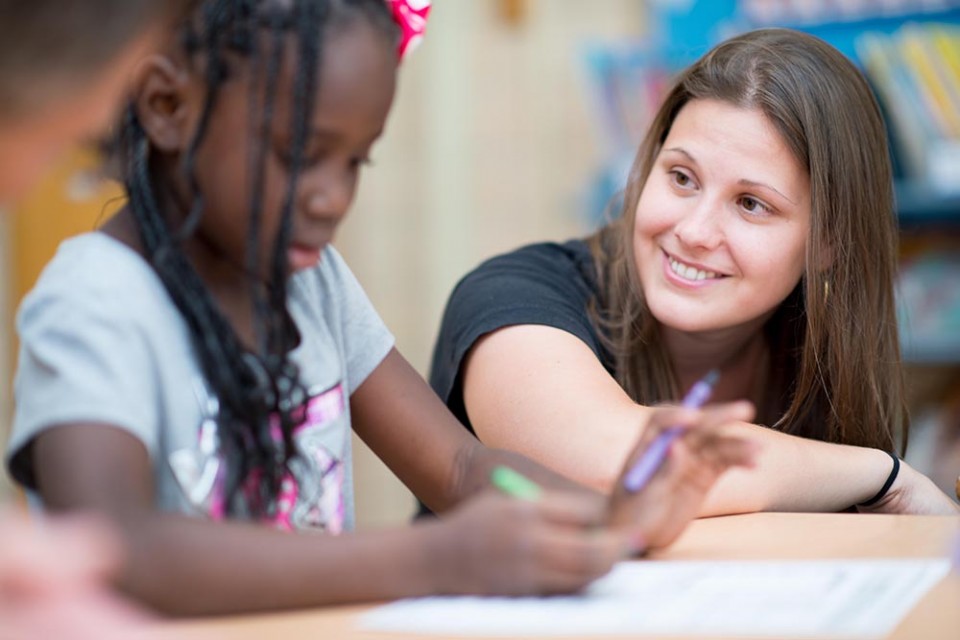 Teacher looking at a girl student while she's coloring.