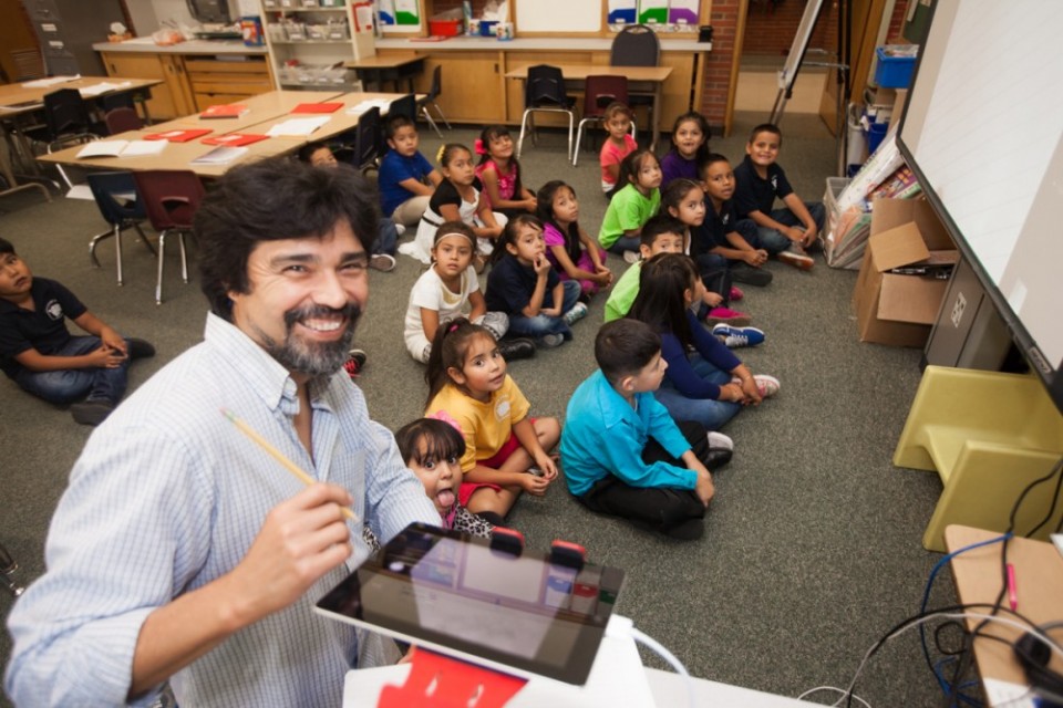 Teacher holding a tablet while a group of kids are sitting on the floor