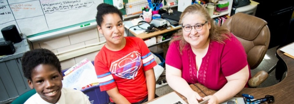 Two young teens and a teacher using laptops sitting on a desk