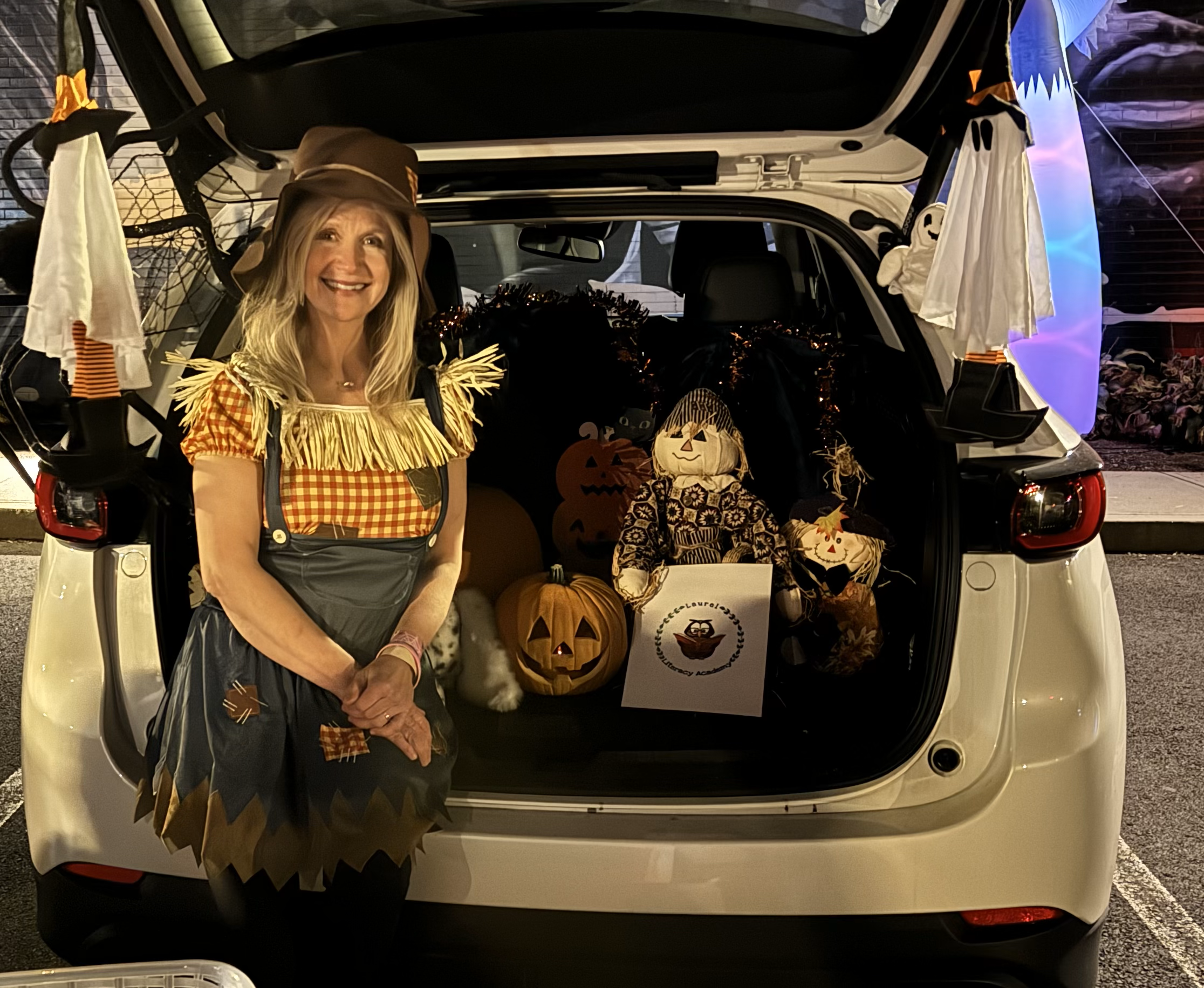 Teacher dressed as scarecrow sitting in trunk fir trunk or treat