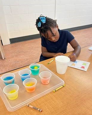 girl at a table in front of cups mixing colors