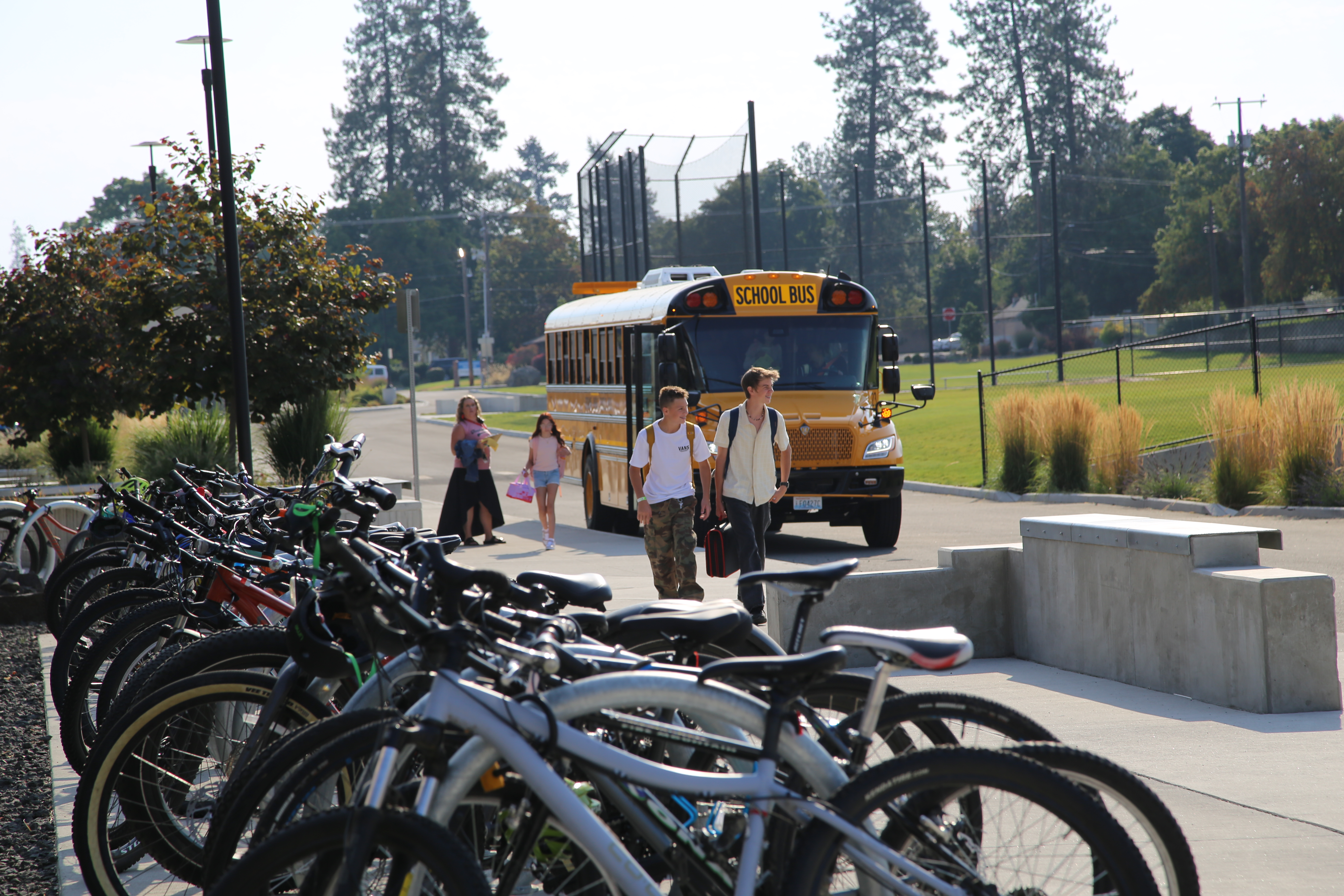 Kids walking to school next to a rack of bikes and in front of a school bus