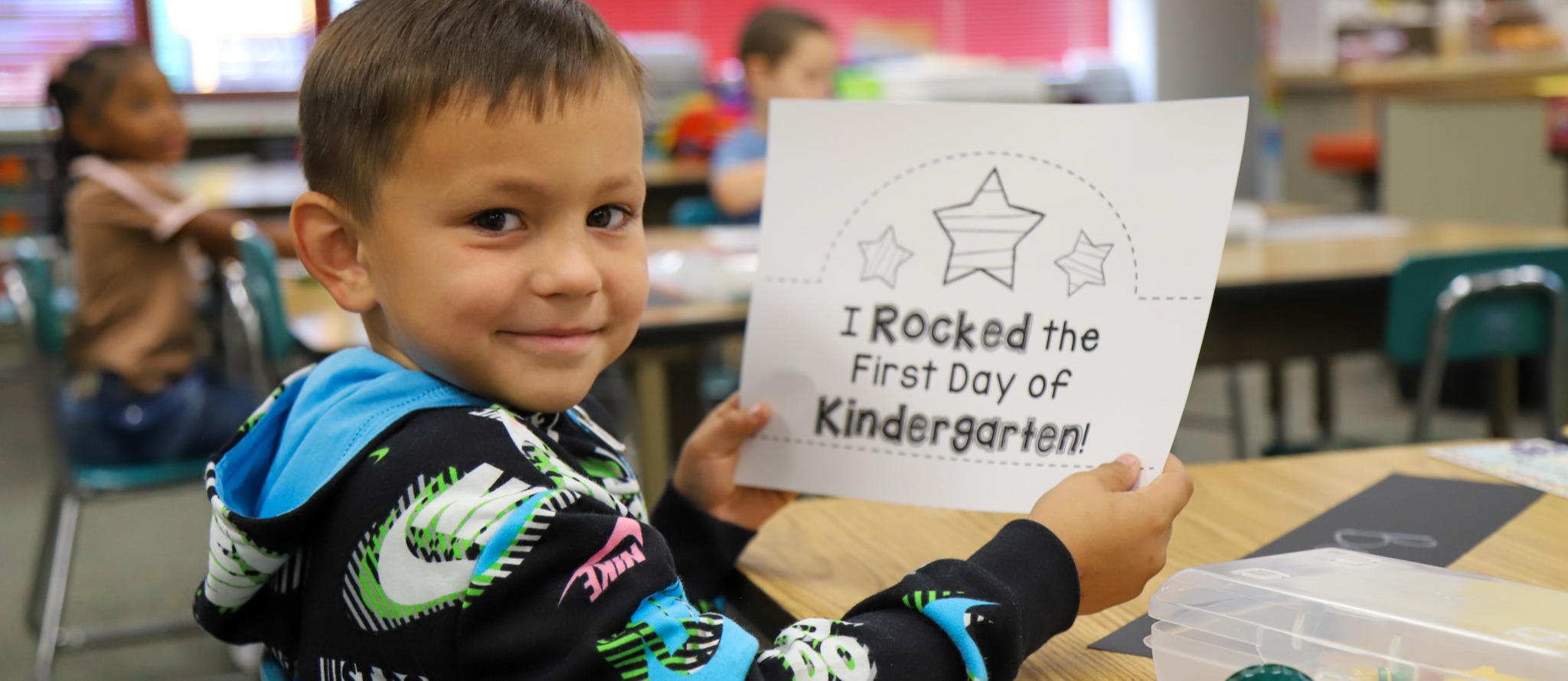 Kid smiling with a sign that says, "I rocked the first day of kindergarten"