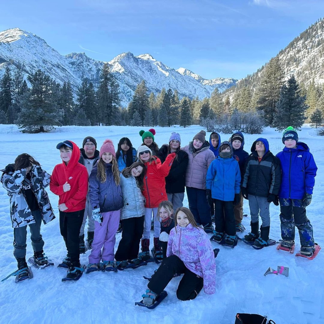 Group of students in snow clothes standing in snow in front of mountain