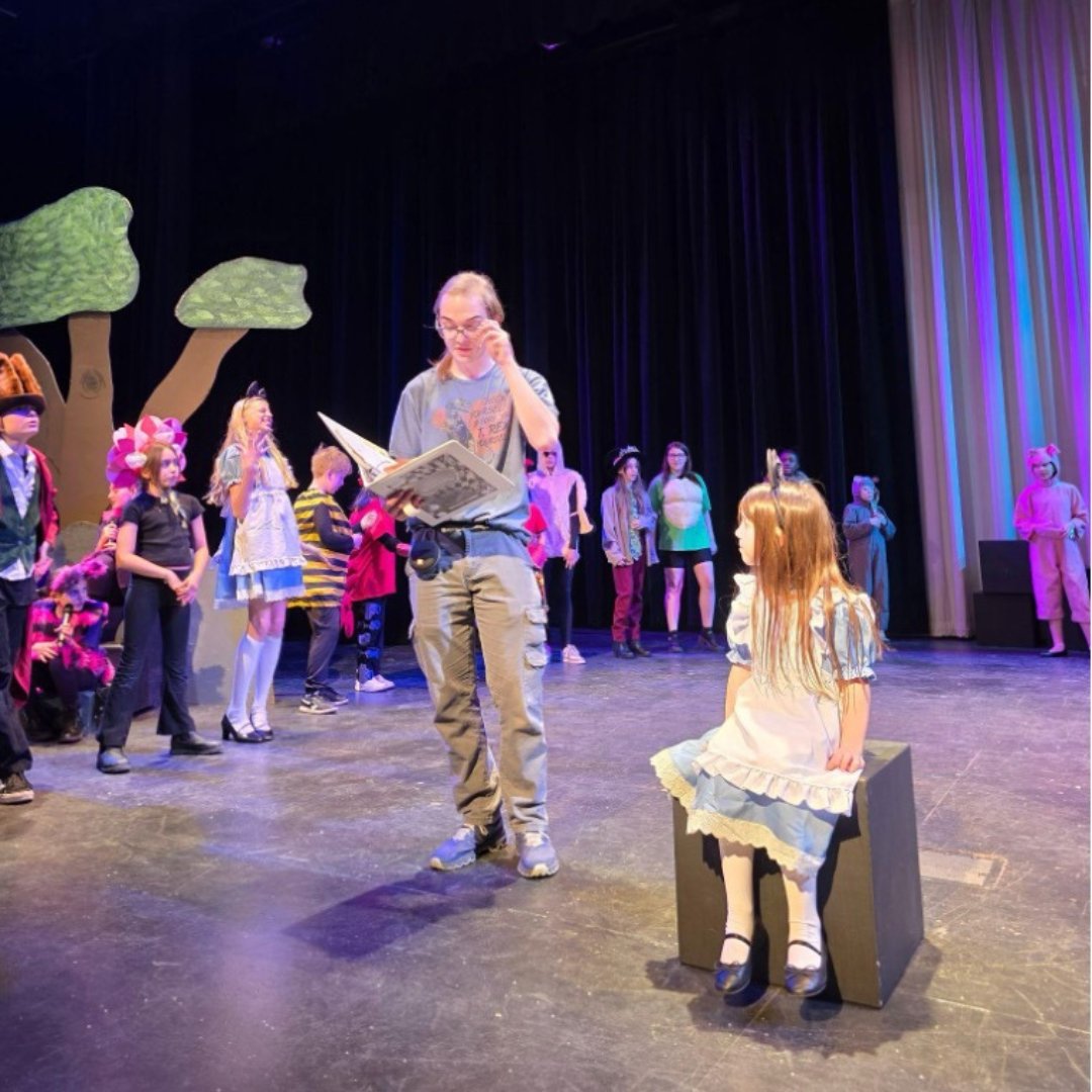 High school student working with elementary school student on stage for theater production