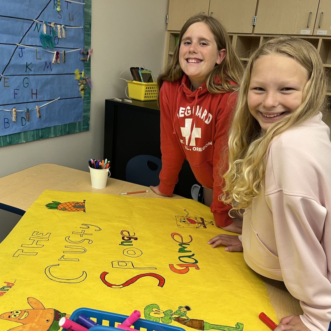 Two girls smiling next to their poster