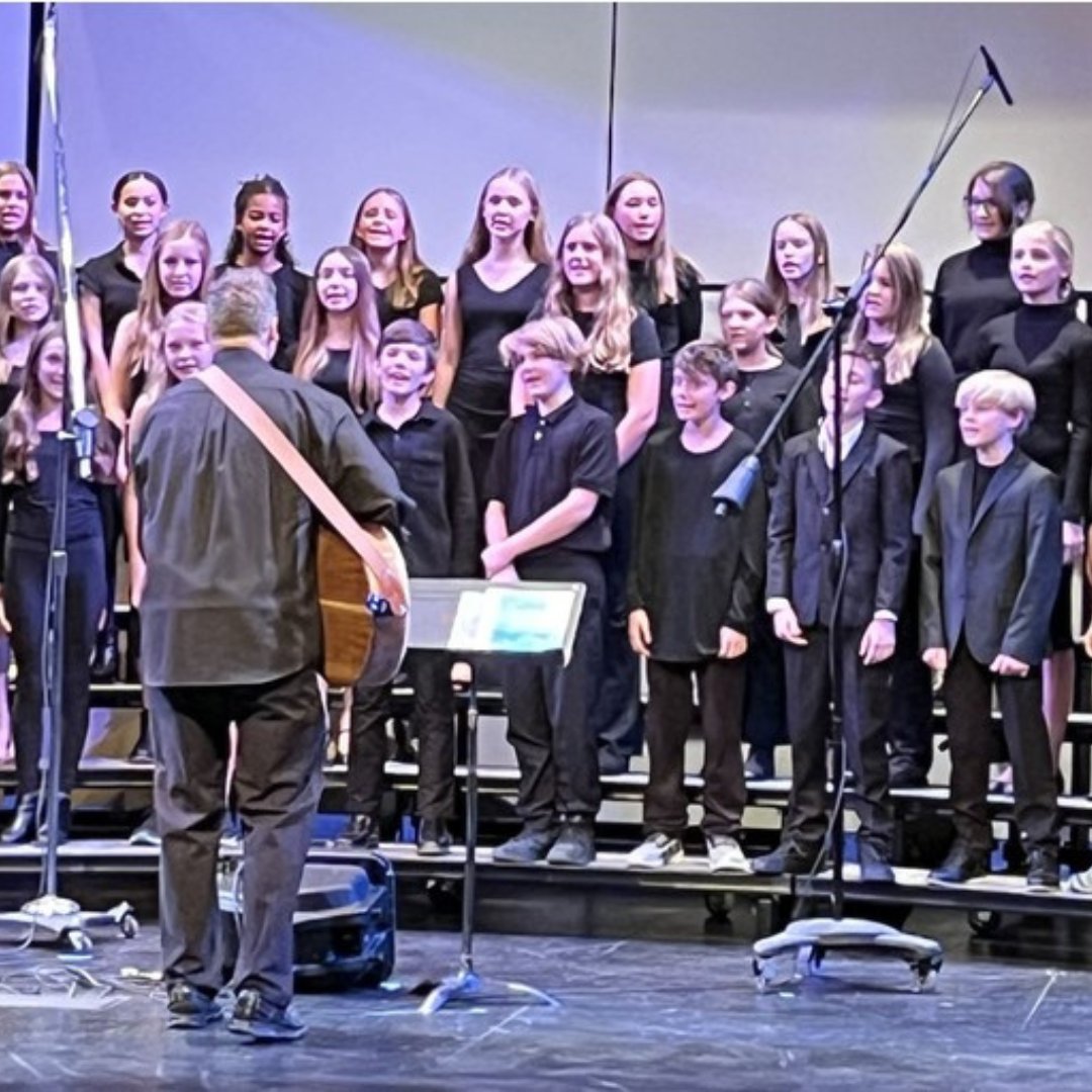 Group of students during a choir performance with teacher in front playing guitar