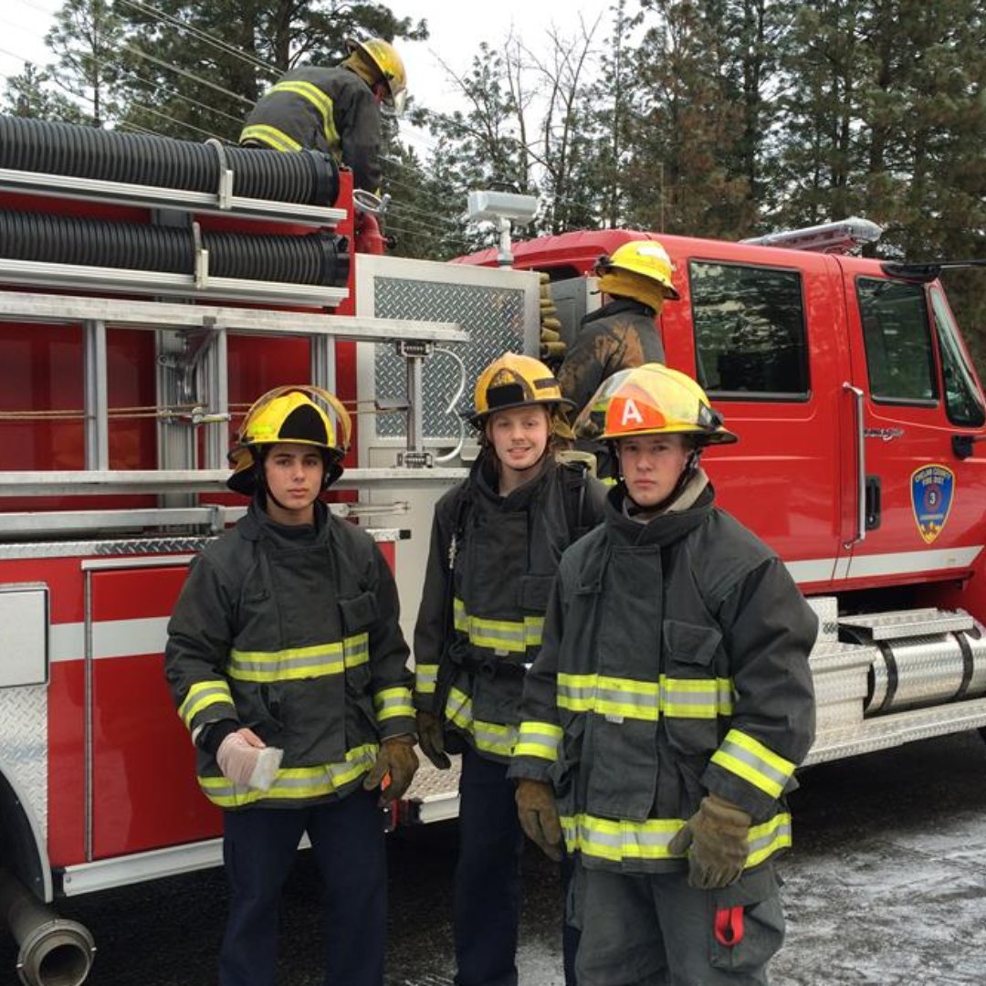 Three students in firefighter gear standing in front of fire truck