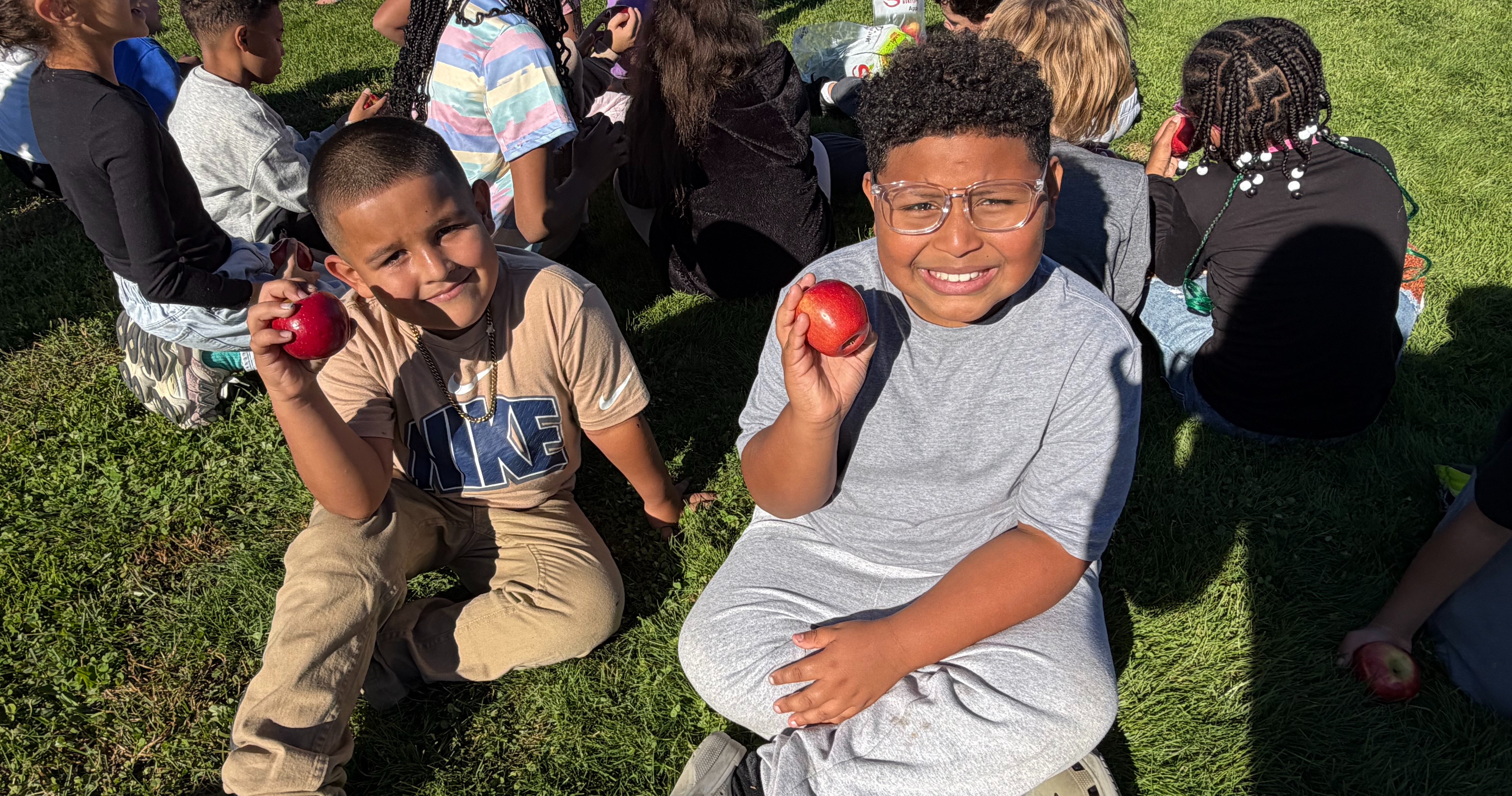 Two students sitting on the ground holding apples