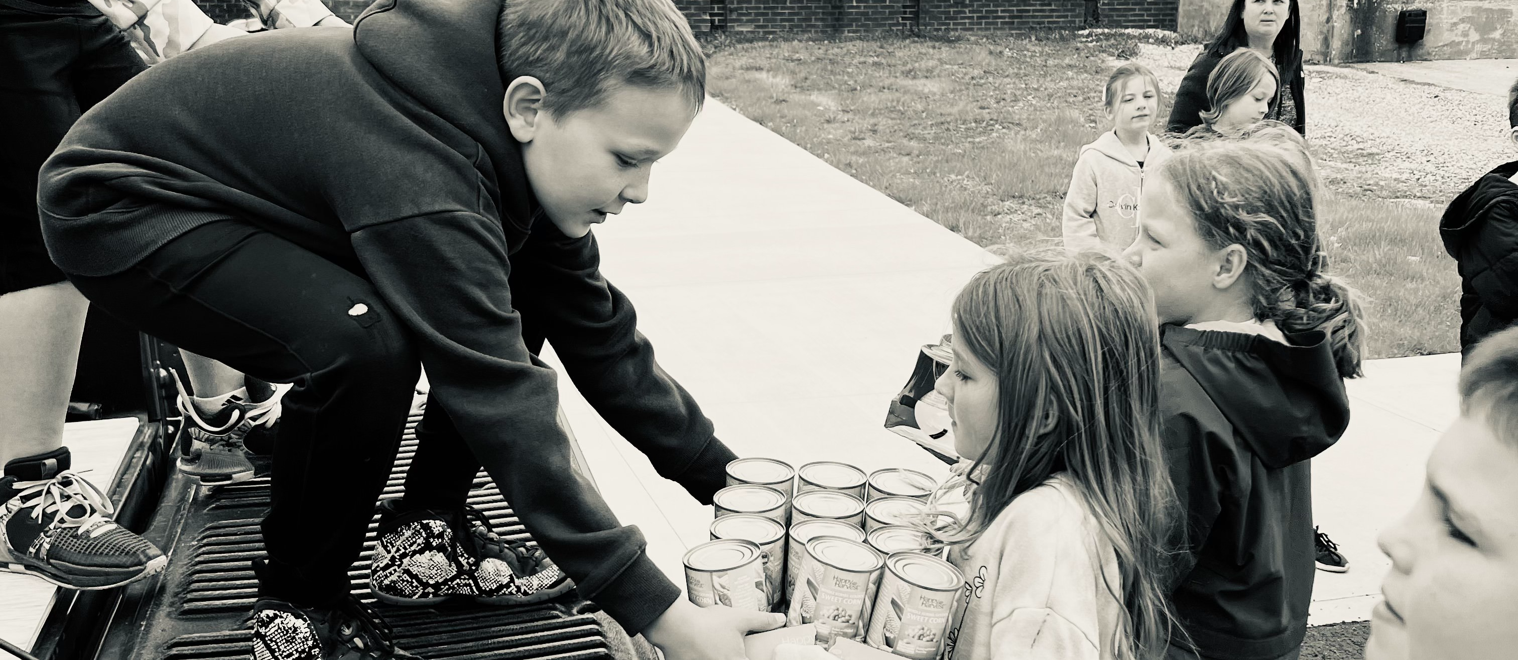Boy on a truck accepting a box of canned goods from a girl