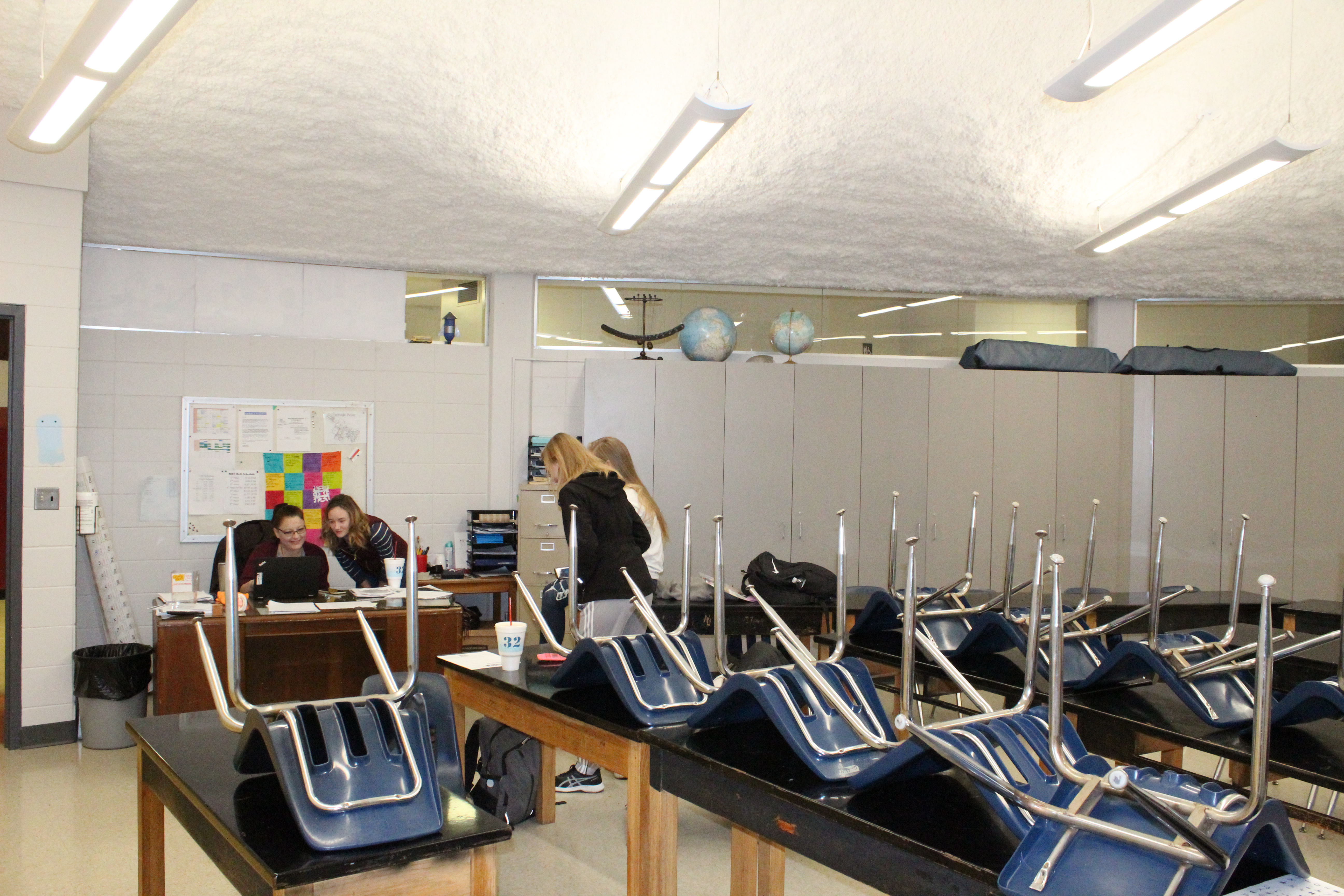 A photo of a classroom with all of their chairs stacked up over their respective desks.