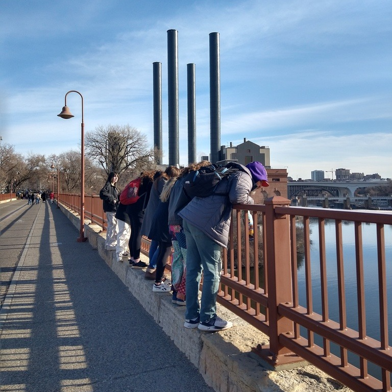 students overlooking a river on a bridge