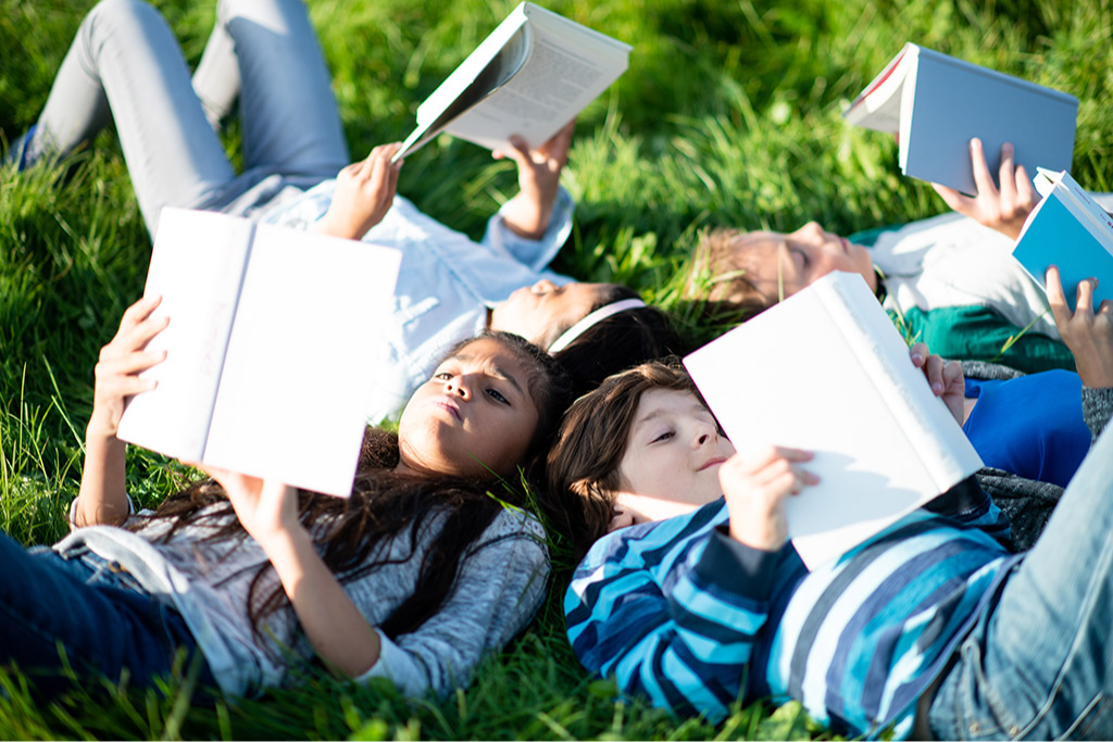 Group of kids lying in the grass reading books together