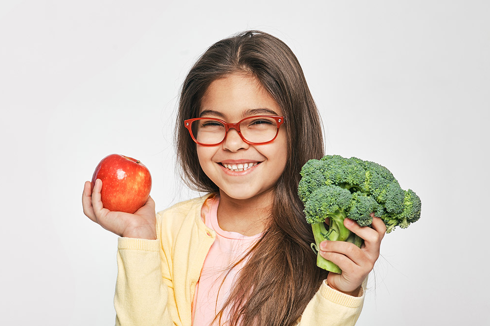 Girl holding an apple and broccoli