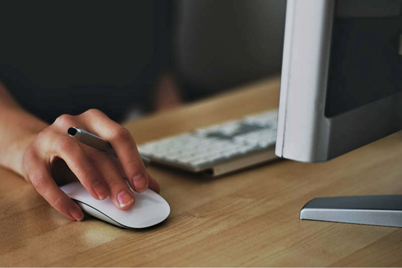 A hand holding a stylus and using a mouse at a desktop computer